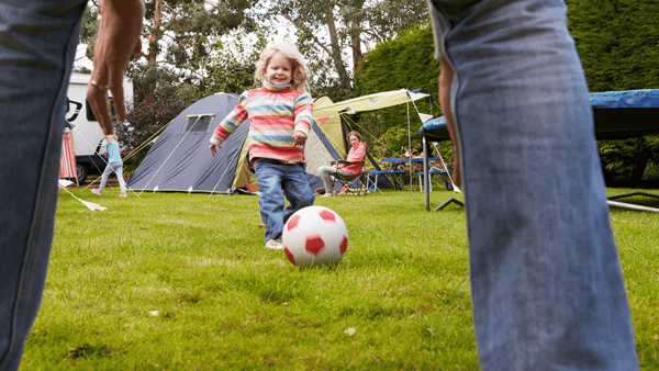 little girl enjoying a game of football while camping