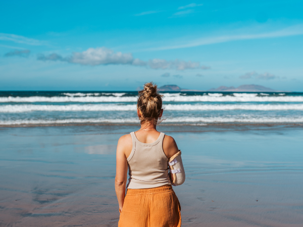 woman stands on a beach looking out at the water with a cast on her right arm